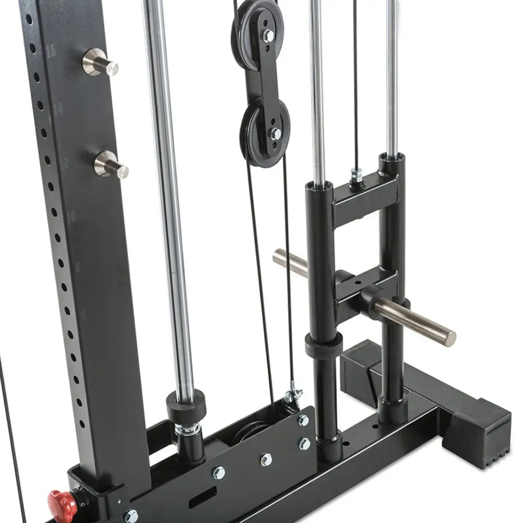 Close-up of a cable machine at a gym. The image shows pulleys, cables, and metal frames, with adjustment pins and a handle. The equipment is designed for weight training and resistance exercises. The setup is sturdy and industrial in design.