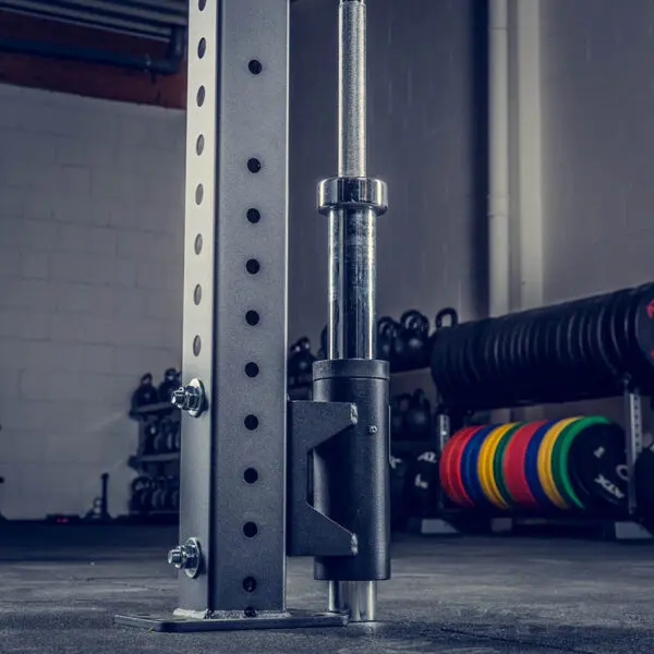 A gym setup with ATX® Barbell Storage showcasing a metal frame, colorful weight plates stacked in the background, kettlebells lined up on shelves, and concrete walls and ceiling.