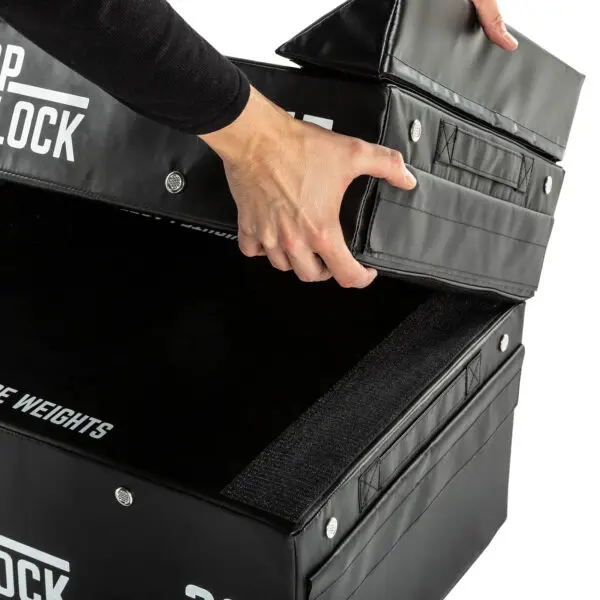 A person stacks ATX® 15 cm Soft Drop Blocks, featuring black padding with Velcro fasteners and branded text.