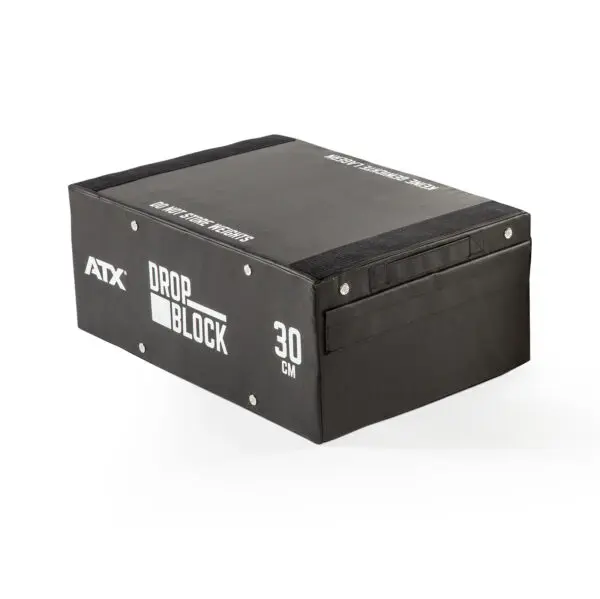 A black rectangular exercise block with white ATX Drop Block 30 cm text, sturdy side panels, and a handle, designed for gym use is known as the ATX® 30 cm Soft Drop Block.