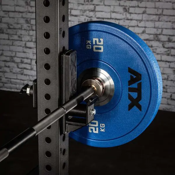 An ATX® Roller J-Hook holds a blue 20 kg weight plate on a barbell, resting on a rack with a brick-patterned wall backdrop.