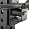 A close-up of an ATX® Roller J-Hooks shows its cylindrical design with a bolt on the side, resting on a weight rack. The black metal J-cup allows for adjustable height placement via multiple rack holes.