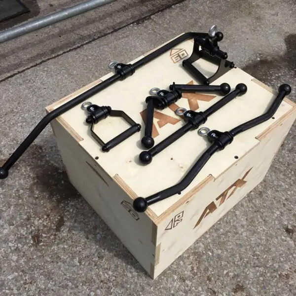 The ATX® V Bar Rotational Blackline, a collection of black metal car parts including sway bars and connectors, is displayed on a wooden crate labeled ATX on a concrete surface.