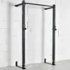 An ATX® Wall Mounted Squat Rack, black and featuring a pull-up bar, is installed on a white brick wall. It has adjustable J-hooks for securing a barbell. The concrete floor is clear of weights and other equipment.