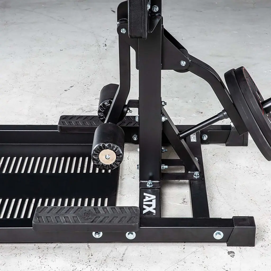 Close-up of a black leg press machine, similar to the robust ATX® Leg Master, with metal plates and padded rollers on a gray concrete floor. Labeled ATX.