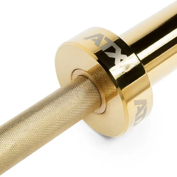 A close-up of the ATX® Olympic Golden Powerlifting Bar reveals its gold-colored, textured grip and shiny cylindrical end engraved with ATX, which reflects light to highlight its metallic finish.
