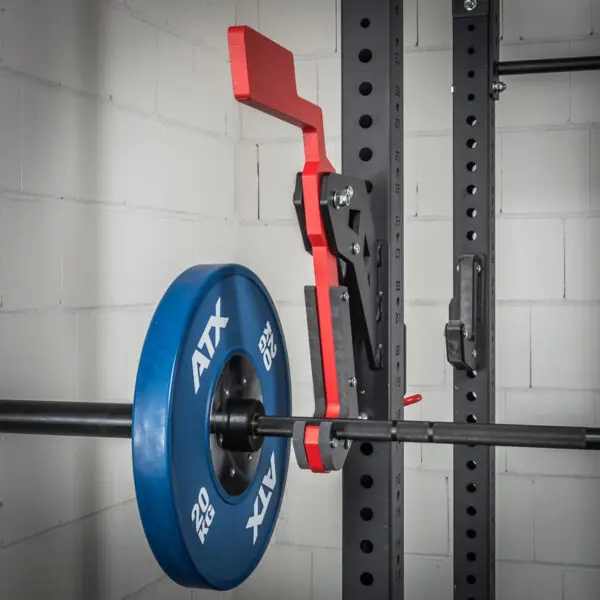 The ATX® Mono Lift, featuring a barbell with blue weight plates and a red lever mechanism, is set against a white brick wall background on a gym rack.
