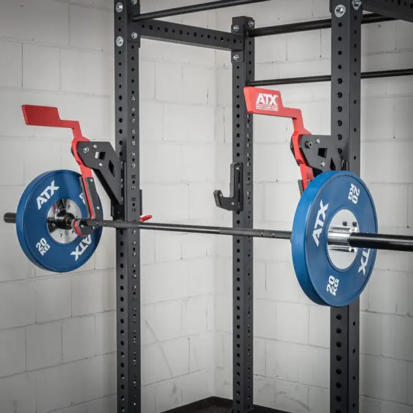 An ATX® Mono Lift with a barbell and blue weight plates is set up in a gym. It features safety catches on both sides. The white walls create a clean, organized workout space.