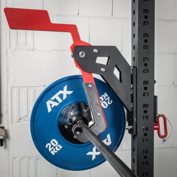 The ATX® Mono Lift in red and black secures a barbell with a blue 20 kg ATX weight plate on a gym rack, set against a white brick wall backdrop. The rack features visible numbered holes.