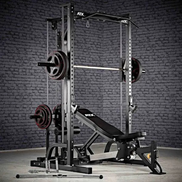 A home gym setup showcasing the ATX® Smith Machine System Plate Loaded, accompanied by a barbell, weight plates, and an adjustable bench, all set against a brick wall backdrop.