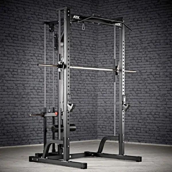 A black ATX® Smith Machine System Plate Loaded is set on a gray floor against a dark brick wall, featuring a pull-up bar, adjustable safety bars, and weight storage pegs.