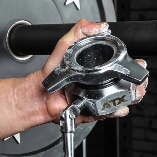 A chalk-dusted hand adjusts an ATX® Competition Powerlifting Collar IPF on a barbell, ensuring the weight plate is secure for stable and safe lifting.