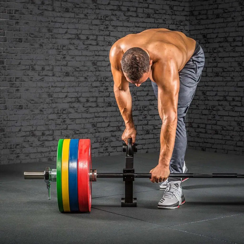 Man with no shirt loading a barbell with bumper plates and a single deadlift jack.