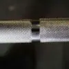 A close-up of the 7ft Olympic Barbell Thrust Bearings 1500lbs highlighting its textured knurling and contrasting shiny metal band against a dark background.