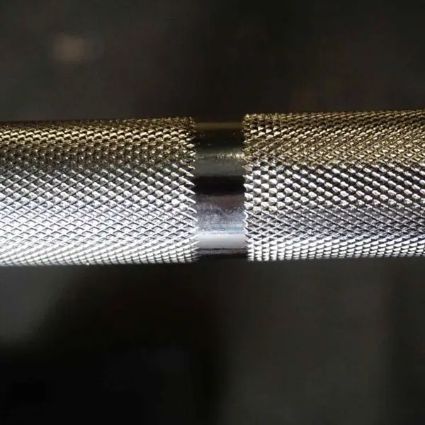 A close-up of the 7ft Olympic Barbell Thrust Bearings 1500lbs highlighting its textured knurling and contrasting shiny metal band against a dark background.
