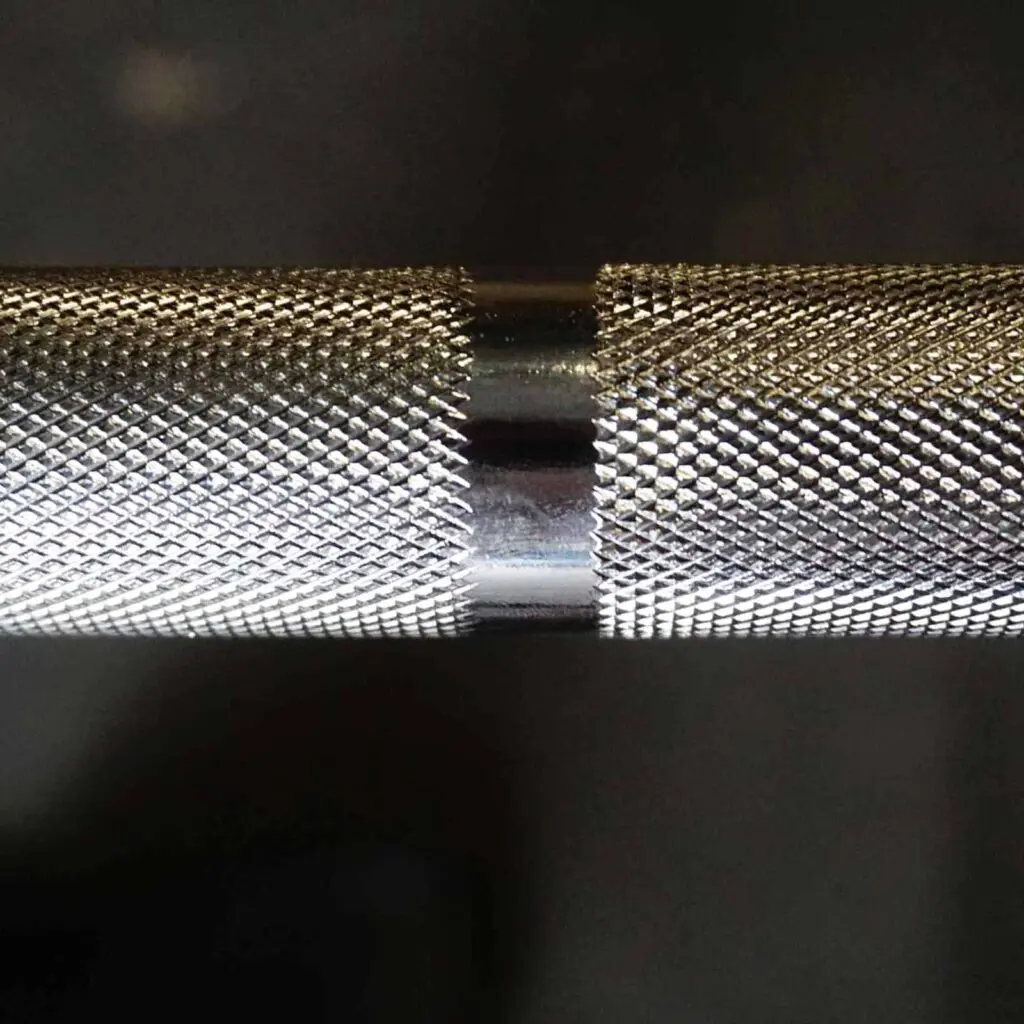 Close-up of a 7ft Olympic Barbell 1000lbs against a dark background, highlighting its textured, knurled grip with an intricate pattern that provides a superior rough surface for enhanced grip.