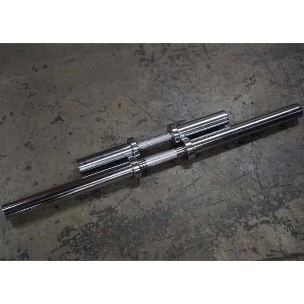 Two Power Maxx Big Olympic Dumbbell Handles lie parallel on a textured concrete floor, their metallic surfaces glinting in the light and featuring smooth, cylindrical sections ready for weights.