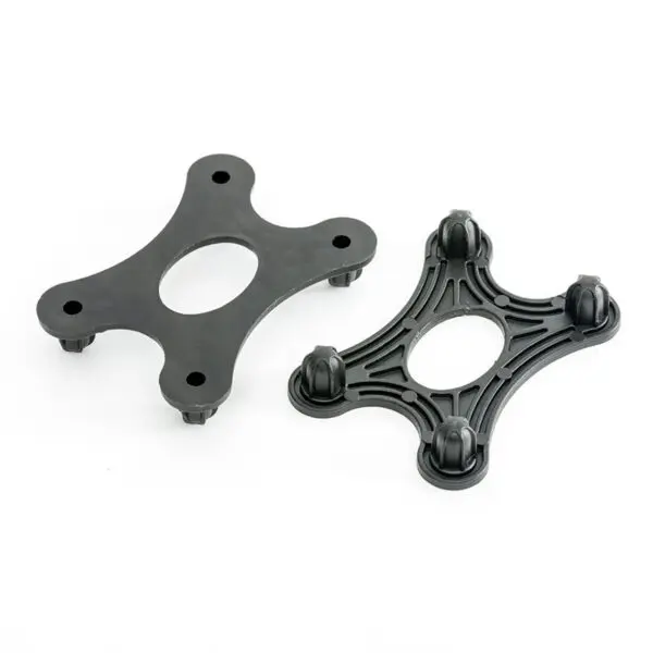 Two black, four-pronged GymFloor® RTS Turf components with oval centers are shown. One is solid with a smooth surface; the other has a grooved design and knobs at each tip. Both sit on a white background.