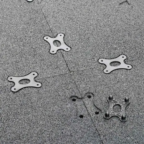 Close-up of GymFloor® RTS Turf 50x50@20mm textured surface with scattered metal brackets featuring a four-hole design. A small indentation is visible near the center.