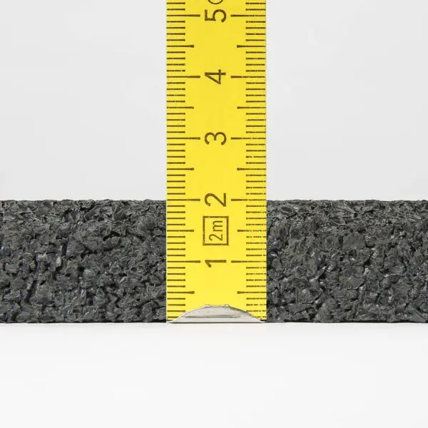 A close-up image of a yellow ruler standing vertically against the textured black surface of a Gymfloor® 20mm 1m x 1m mat, with the rulers measurements showing the black material is approximately 2.5 inches (6.5 centimeters) tall.
