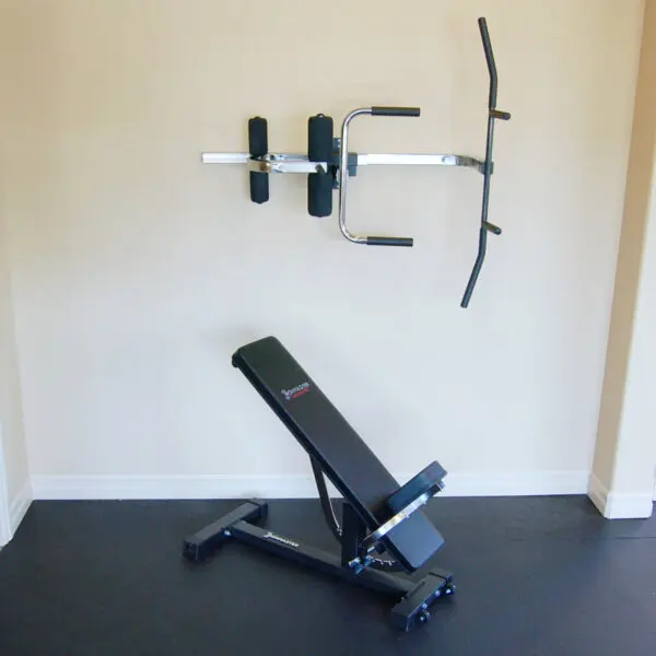 A minimalist home gym setup features the Ironmaster Ultimate Chin Up Attachment for the IM2000 and an adjustable weight bench below, complemented by neutral-colored walls and a dark floor mat.