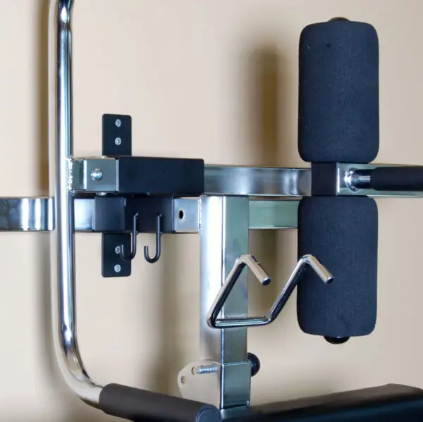 Ironmaster Ultimate Chin Up Attachment for IM2000 against a beige wall, featuring a chrome and black frame with padded supports and handles for exercises like leg curls or extensions.
