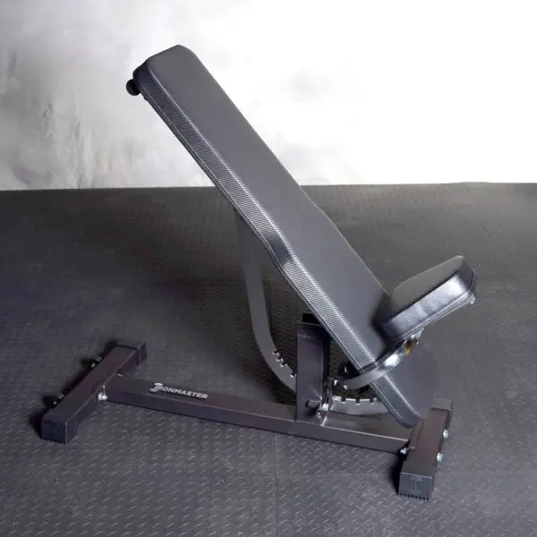 The Ironmaster Hybrid Bench Pad, a black adjustable weight bench with a comfortable padded seat and backrest, is inclined and stable on a textured dark gym floor.