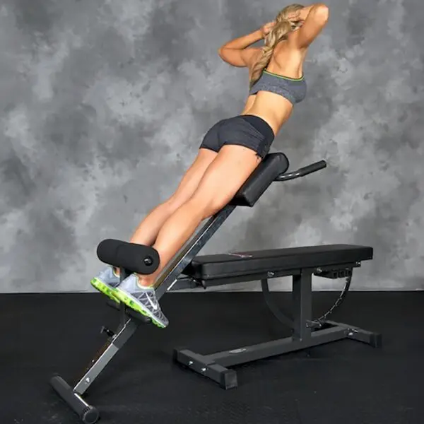 A person using the Ironmaster Hyper Core Attachment for back extensions, wearing a gray sports top, black shorts, and green athletic shoes against a plain, textured gray wall.