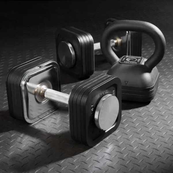 A set of adjustable dumbbells with black square plates and the Ironmaster Adjustable Kettlebell Handle rests on a textured rubber gym floor. The equipment features a modern design, ideal for strength training exercises.