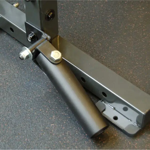 The Ironmaster Landmine Attachment, in black metal, is securely attached to a gym rack on a dark speckled floor. This versatile sleeve device enhances barbell exercises for dynamic strength routines.