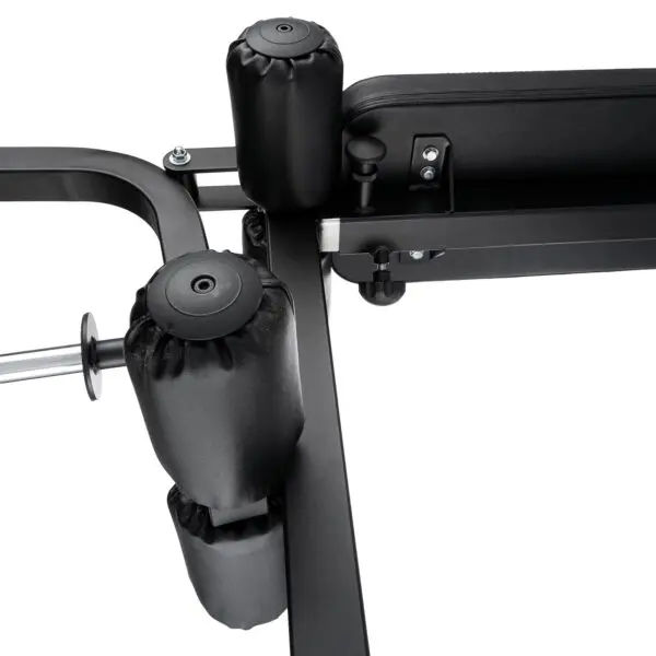 Close-up of the Ironmaster Leg Lift PRO, highlighting its padded rollers and bench. The focus is on the padding and robust metal frame that emphasize its construction and design features.