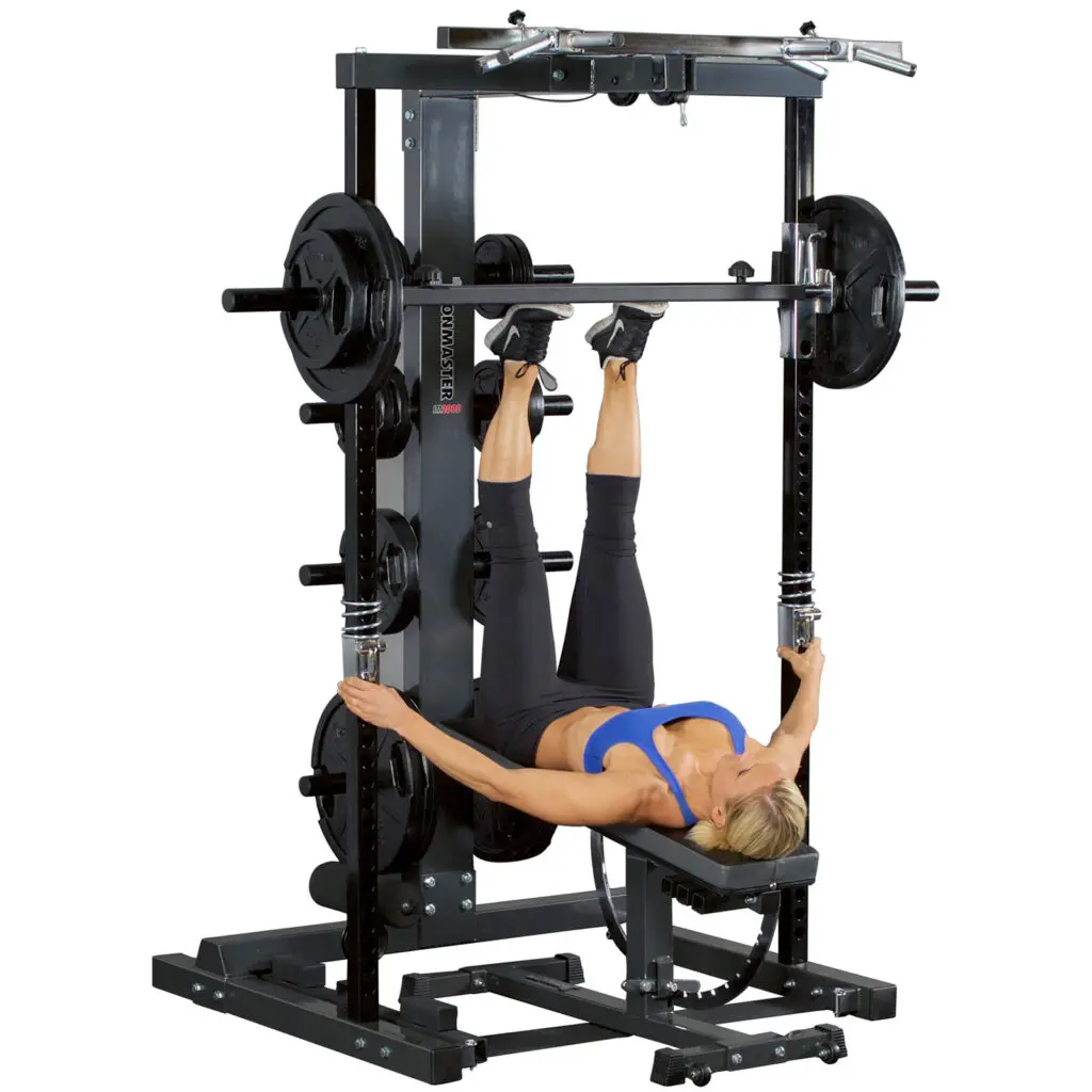 Someone in athletic wear performs an upside-down exercise using the Ironmaster Leg Press Plate for IM2000, gripping a bar with both hands. The setup includes weight plates and a bench.