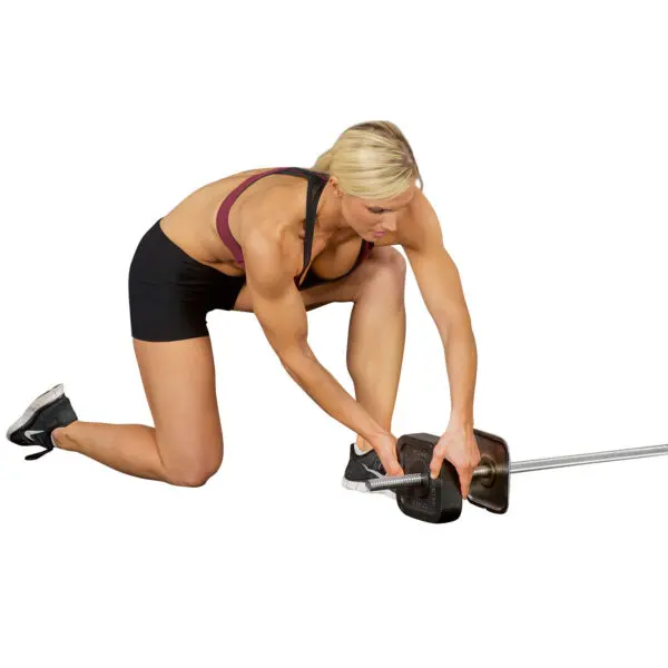 Kneeling on one knee, a person adjusts the weights on an Ironmaster Straight Barbell, clad in workout gear featuring a black sports bra and shorts. The plain white background highlights both the individual and the barbell.