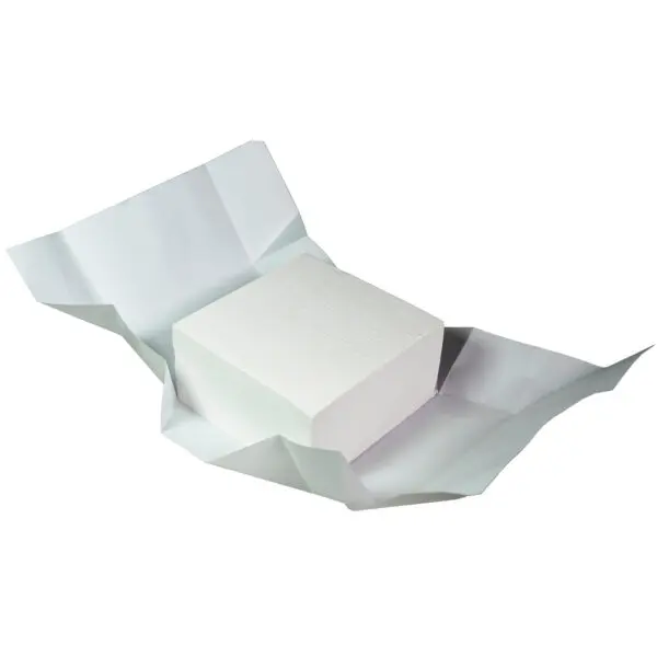 A white block of butter paper sits partially unwrapped on a flat surface, resembling a chalk box. The paper is creased and unfolds around the rectangular block, showcasing the texture and thickness. The plain white background completes the minimalist scene.
