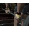 A person grips a barbell using the Spud Inc Fat Triceps Strap, readying for a deadlift in the gym. Their hands and legs are in focus, with gym equipment visible in the background.