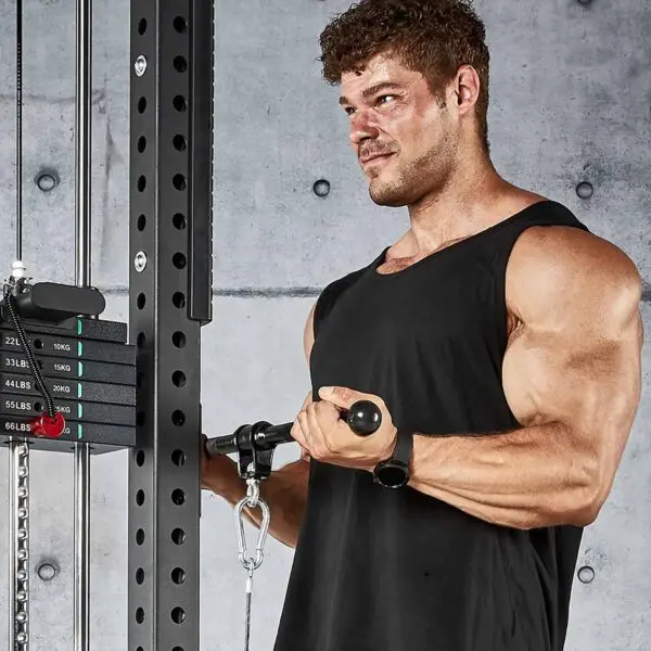 A muscular man in a black tank top does cable curls with an ATX® Straight Bar Rotational Blackline, focused against a concrete wall with a weight stack visible beside him.