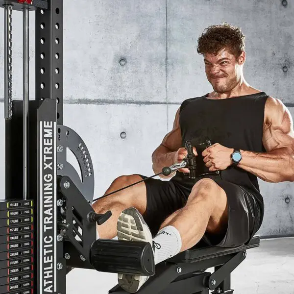 A person wearing a black tank top, dark shorts, white socks, and athletic shoes is focused while using the ATX® Cable Row Handle Blackline on a rowing machine in front of a concrete wall.