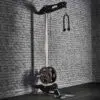 The ATX® Wall Mounted Lat Pulldown boasts a sleek black metal frame, weight plates, and a double-handle grip. It is ideally positioned against a textured gray brick wall in a gym setting, providing both functionality and style for an intense workout experience.