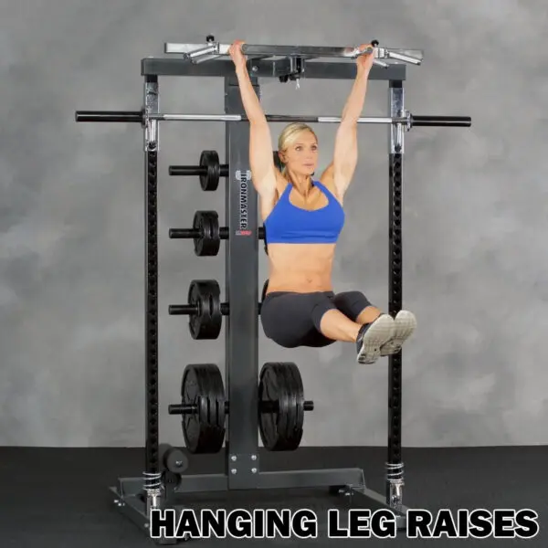A woman in athletic wear performs hanging leg raises on a pull-up bar attached to an Ironmaster IM2000 Self-Spotting Smith Machine, lifting her legs horizontally. The text HANGING LEG RAISES is displayed at the bottom.