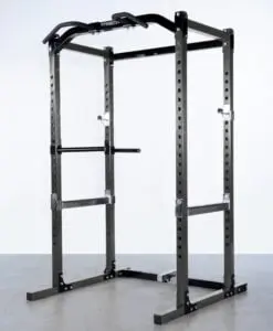 A black power rack for weightlifting standing on a gray floor. It features adjustable safety bars, a pull-up bar, and dip handles, all designed for strength training exercises.