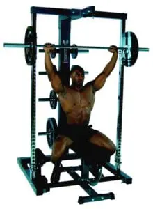 A person performs a shoulder press exercise using a barbell on a seated rack machine. The person appears focused and is in a gym setting, showcasing a weightlifting routine.
