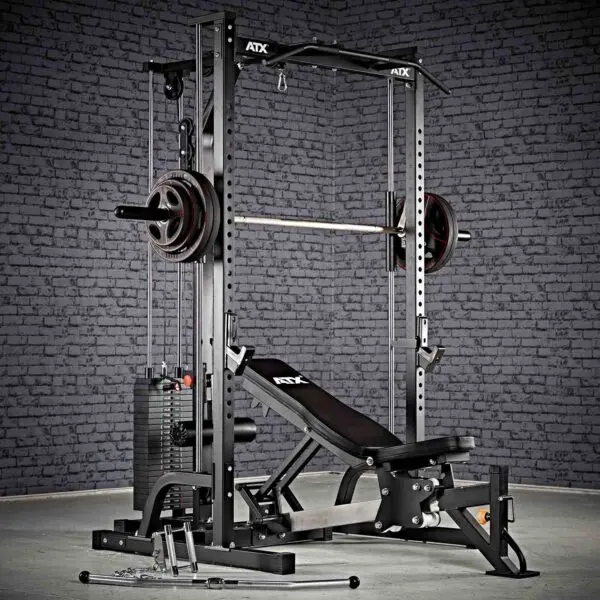 Against a brick wall, the ATX® Smith Machine System Stack Weight 115 kg offers multi-functional home gym equipment, featuring a bench press, adjustable weight rack, and attachments like cables and bars for diverse workout routines.