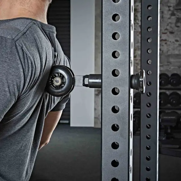 A person uses the ATX® Mobility Roller attached to a gym rack for their upper back. They wear a gray shirt, and exercise equipment and weights are visible in the background.