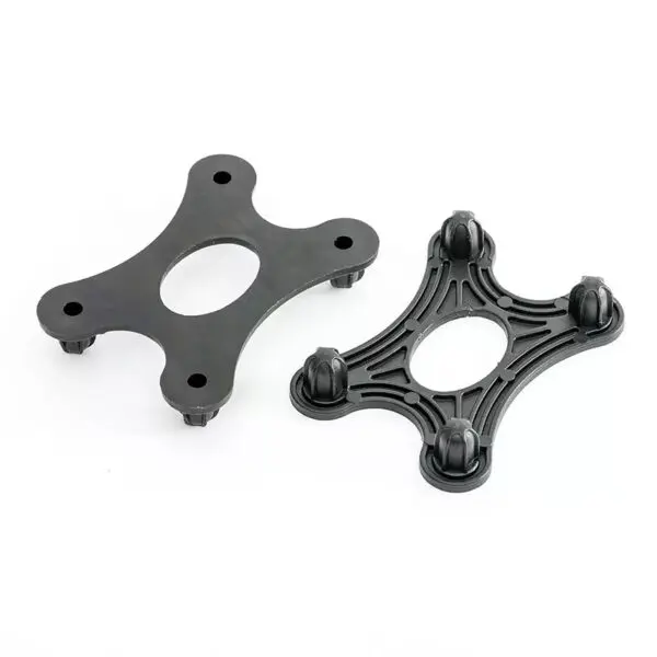 Two black plastic spider strainer connectors with four prongs and a central oval opening from the GymFloor RTS 50x50@20mm System are displayed. One shows the top view, while the other displays the underside with prongs visible against a white background.