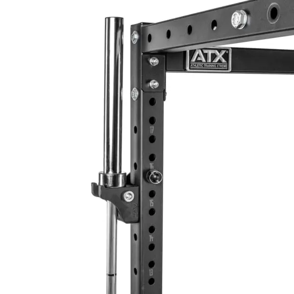 Close-up of the ATX® Bar Holder, a black metal squat rack featuring multiple holes and a chrome barbell. The ATX Athletic Training Xtreme logo is visible, with a secured clip holding the barbell in place.