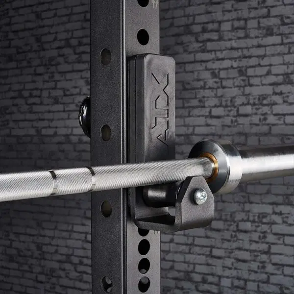 Close-up of an ATX® Roller J-Hooks Universal barbell on a black rack with adjustable holes and ATX branding, set against a textured gray brick wall.