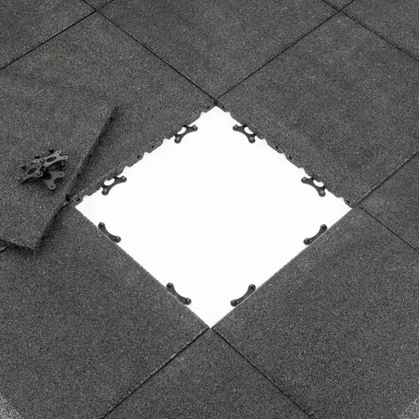 View of Shock & Sound Tile 30mm System in dark gray, with one tile partially removed to reveal a white surface underneath. A corner piece lies on the side, highlighting the tiles textured surface and connector designs.
