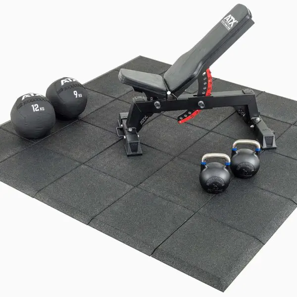 A gym setup with an adjustable black bench on Shock & Sound Tile 30mm System flooring, along with two kettlebells and two weighted medicine balls.