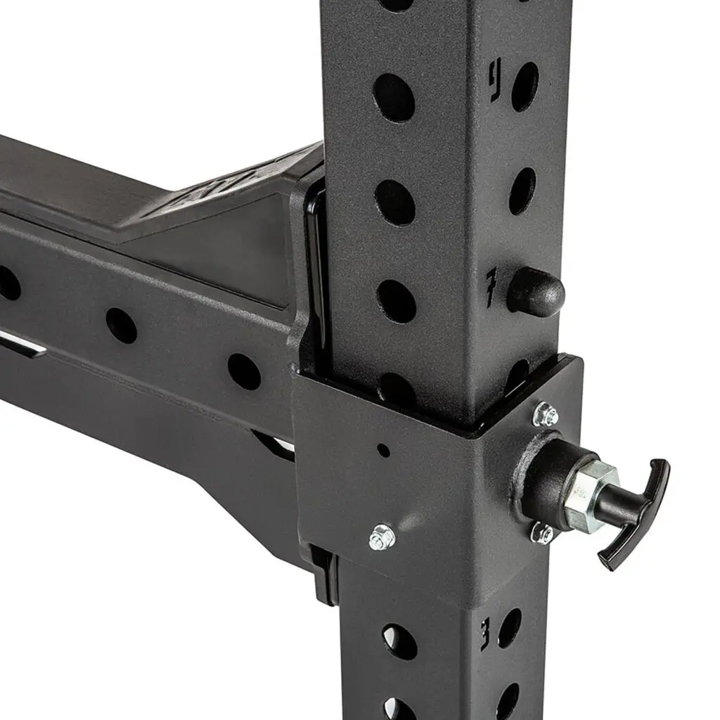 Close-up of a black metal exercise equipment frame with multiple adjustment holes and a secure locking mechanism with a knob. The construction appears sturdy and industrial, designed for a fitness or gym setting.