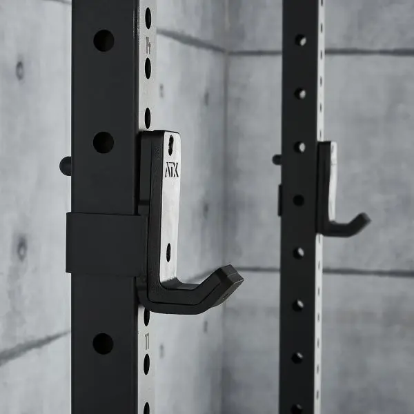 Close-up of the ATX® Power Rack 770 XL SET, a black steel squat rack with adjustable hooks. It features holes and numbering for height adjustments, set against a gray concrete wall in a modern minimalist gym.